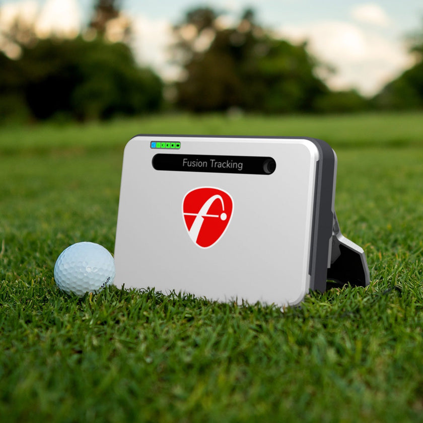 FlightScope Mevo+ Launch Monitor on grass near golf ball, showcasing Fusion Tracking technology for precision golf data analysis.