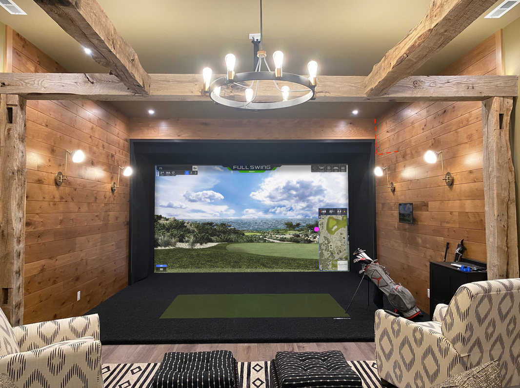 Full Swing Golf home golf simulator package in a wood paneled room with impact screen turf mat and seating