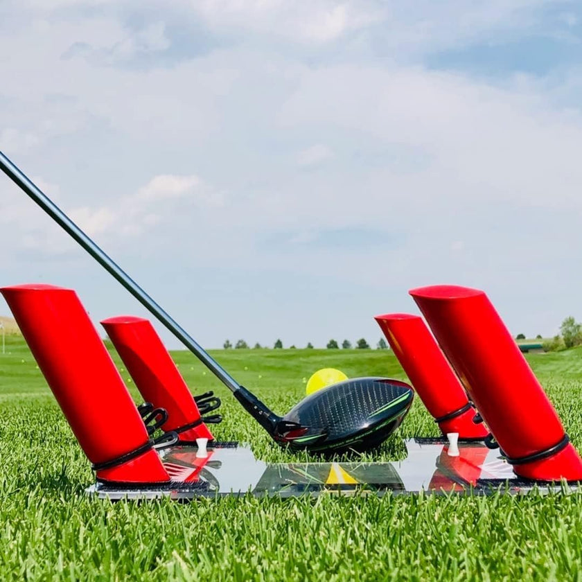 Speed Trap swing trainer with red angled guides and driver head on grassy range with golf ball